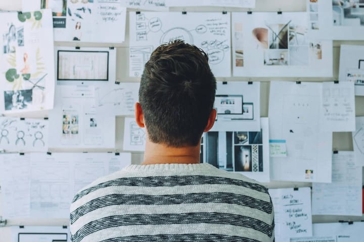Person studying a wall covered in documents and information, representing the research and analysis required before making the enterprise AI build versus buy decision.